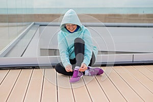 Caucasian woman in a hoodie tying her shoelaces before jogging.