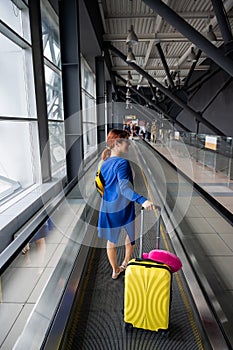 Caucasian woman on a horizontal escalator with a suitcase at the airport. A girl with pink luggage rides on a moving