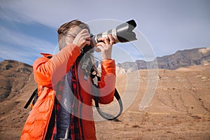 Caucasian woman landscape photographer with big lens and professional camera takes pictures in mountains against