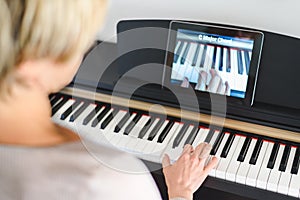 Caucasian woman learning to play piano with video lessons.