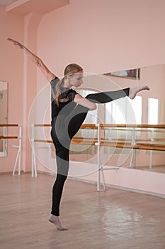 Caucasian woman lifts her leg into a split in a dance hall with a ballet barre. Vertical photo.