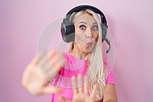 Caucasian woman listening to music using headphones afraid and terrified with fear expression stop gesture with hands, shouting in