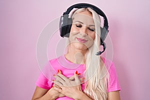 Caucasian woman listening to music using headphones smiling with hands on chest with closed eyes and grateful gesture on face