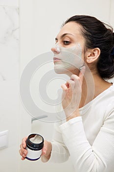 Caucasian woman looking in mirror and applying face mask