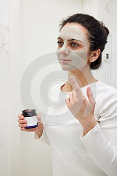 Caucasian woman looking in mirror and applying face mask