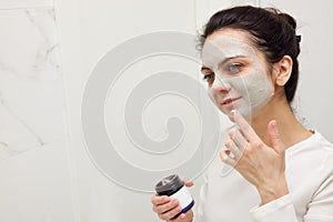 Caucasian woman looking in mirror and applying face mask
