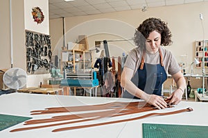 Caucasian woman makes belts from genuine leather in a workshop.