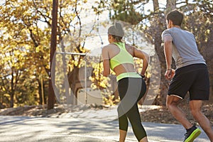 Caucasian woman and man jogging on a country road, back view