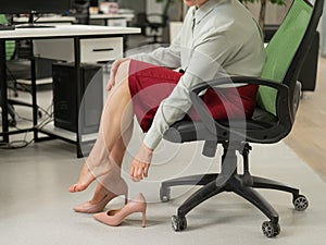 Caucasian woman massaging her tired legs while sitting in the office. Cropped.