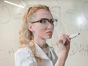 A Caucasian woman in a medical gown thinks and finalizes formulas on a transparent wall. photo