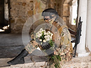 Caucasian woman in military uniform holding a machine gun and a bouquet of white roses.