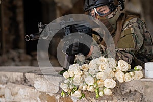 Caucasian woman in military uniform holding a machine gun and a bouquet of white roses.