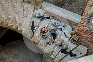 Caucasian woman in military uniform lies on the stairs of an abandoned building and holds a machine gun. View from above