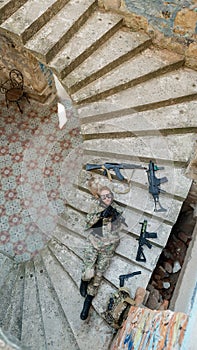 Caucasian woman in military uniform lies on the stairs of an abandoned building and holds a machine gun. View from above