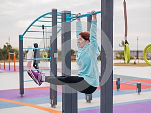 Caucasian woman in a mint sweatshirt hangs on a horizontal bar and does an exercise of the abdominal muscles on the