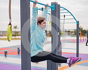 Caucasian woman in a mint sweatshirt hangs on a horizontal bar and does an exercise of the abdominal muscles on the