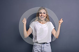 Caucasian woman in neutral casual outfit standing on a neutral grey background. Portrait with emotions: happiness, amazement, joy