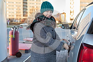 Caucasian woman opening cap lid of car tank on petrol station, winter season, female looking at camera