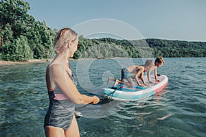 Caucasian woman parent riding kids children boys on paddle sup surfboard in water.