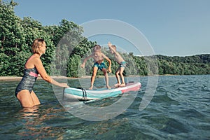 Caucasian woman parent riding kids children boys on paddle sup surfboard in water. Modern outdoor summer fun family activity.