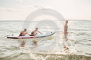 Caucasian woman parent riding kids children boys on paddle sup surfboard in water.