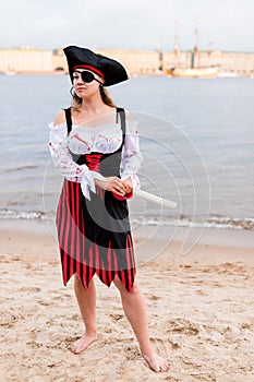 Caucasian woman in pirate costume with eye patch, cocked hat, sword on beach