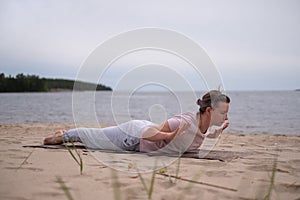 Caucasian woman practicing yoga, doing Salabhasana pose variation on beach
