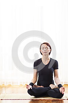 Caucasian Woman Practicing Yoga Indoors. Sitting in Sukhasana Pose Indoors.In Front of Big Sunny Window