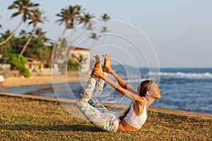 Caucasian woman practicing yoga at seashore of tropic ocean