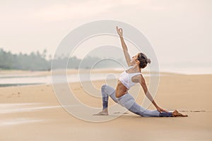 Caucasian woman practicing yoga at seashore of tropic ocean