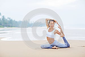 Caucasian woman practicing yoga at seashore of tropic ocean