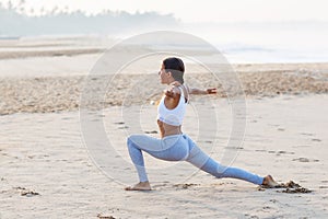 Caucasian woman practicing yoga at seashore of tropic ocean