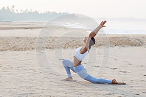 Caucasian woman practicing yoga at seashore of tropic ocean