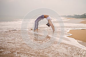 Caucasian woman practicing yoga at seashore of tropic ocean