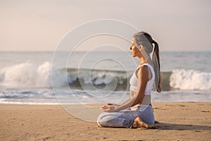 Caucasian woman practicing yoga at seashore of tropic ocean