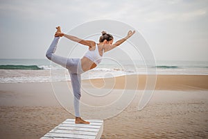 Caucasian woman practicing yoga at seashore of tropic ocean