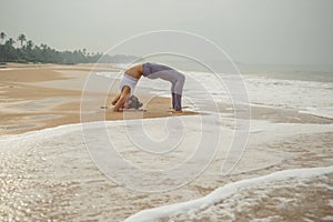 Caucasian woman practicing yoga at seashore of tropic ocean