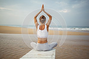 Caucasian woman practicing yoga at seashore of tropic ocean