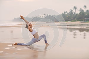 Caucasian woman practicing yoga at seashore of tropic ocean