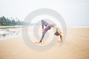 Caucasian woman practicing yoga at seashore of tropic ocean