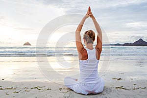 Caucasian woman practicing yoga at seashore of tropic ocean