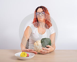 Caucasian woman prefers healthy food and refuses fast food. Redhead girl chooses between broccoli and donuts on white