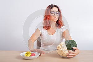 Caucasian woman prefers healthy food and refuses fast food. Redhead girl chooses between broccoli and donuts on white