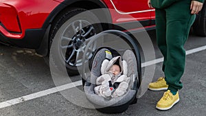 A Caucasian woman puts a child seat with a newborn baby in the car. Quick fastener.