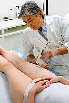 Caucasian woman receiving laser treatment at the leg from a male