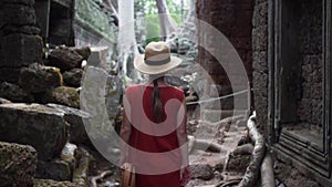 Caucasian woman in red dress is walking among ruins of Ta Prohm