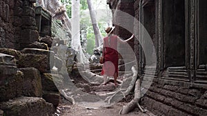 Caucasian woman in red dress is walking among ruins of Ta Prohm