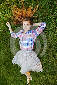 Caucasian woman with red messy hair lying on grass in plaid shirt and tulle tutu skirt. View from above top