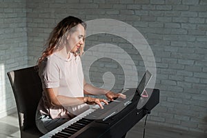 Caucasian woman remotely teaches electric piano playing via video communication on a digital tablet