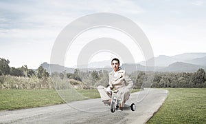 Caucasian woman riding kid`s bicycle on road